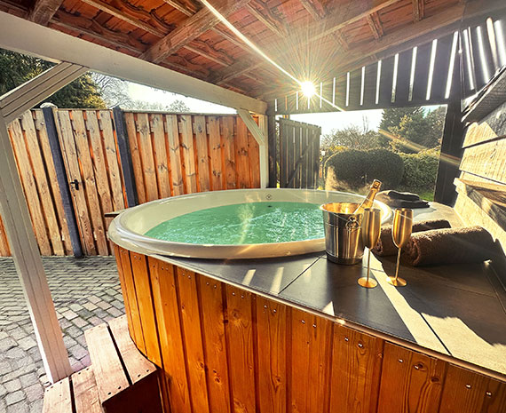 Hotttub met een koeler met fles prosecco en 2 goudkleuige champagne flutes met uitzicht op de wellness tuin door de openslaande luiken