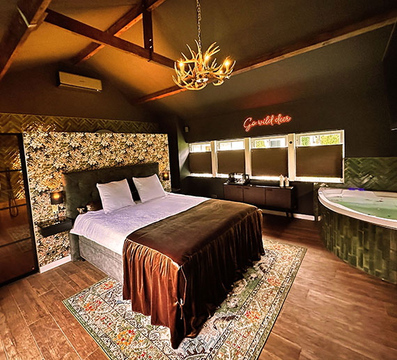 de sint hubertus suite in 1 oog opslag. Riant bed van Swiss Sense dat op een sfeervoel vloerkleed staat. Het hoofdboard van het bed staat tegen een met bloemetjes behangen muur. Achter deze muur bevind zich een badkamer Links van het bed is een grote douchewand waardoor je vanuit het slaapgedeelte de doucheruimte in kan kijken. Tegenover het bed is een gashaard. In de hoek staat een riant 2 persoonsbad met de mogelijkheid tot bubbels. Onder de 4 ramen met uitzicht op de tuin staat een dressoir met een hospitality tray met een nespresso apparaat en voldoende koffie cups en thee.